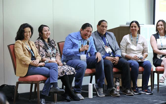 Adults sitting in chairs at a conference. One with a microphone in hand